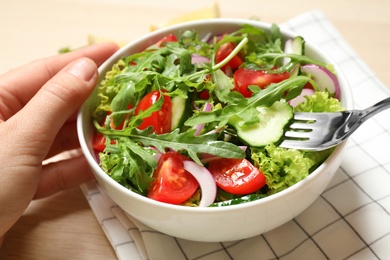 Woman eating delicious salad with arugula and vegetables at wooden table, closeup