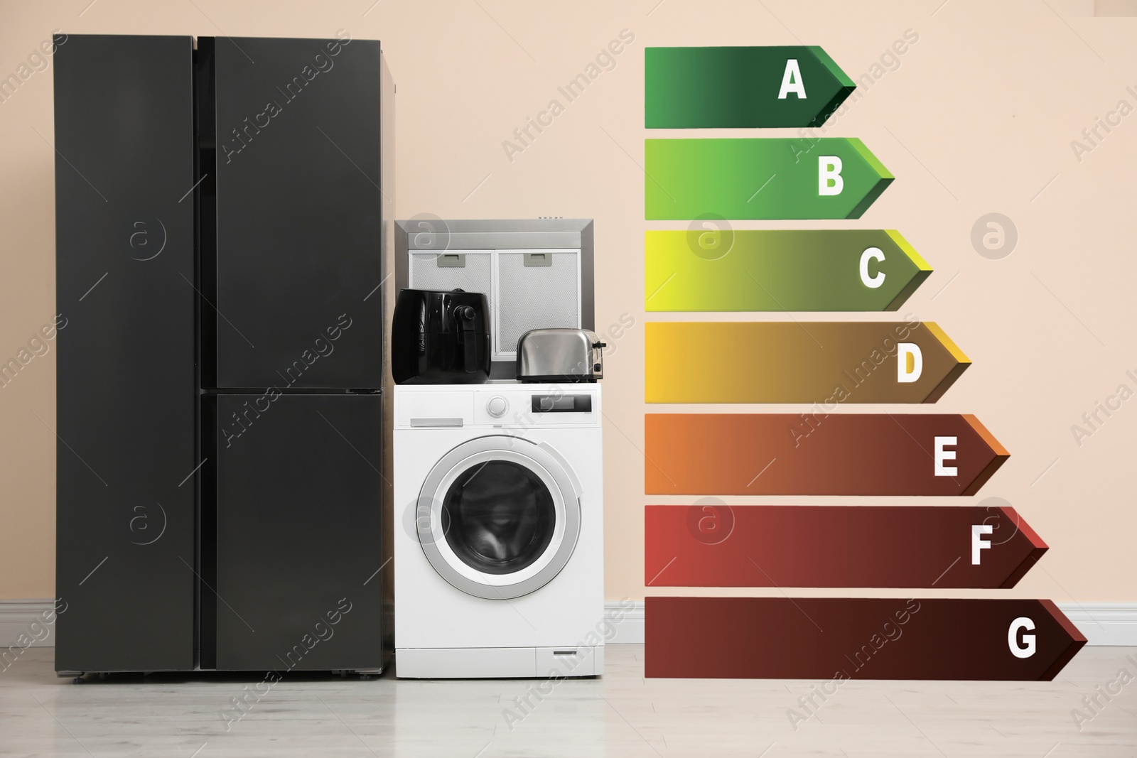 Image of Energy efficiency rating label and different household appliances near beige wall indoors