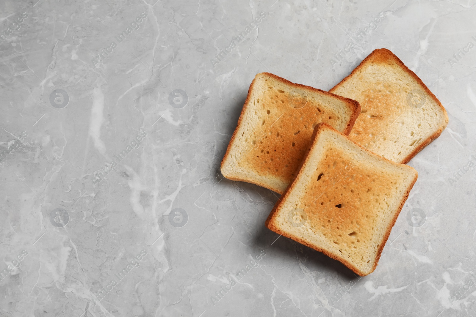 Photo of Slices of delicious toasted bread on gray marble table, top view. Space for text