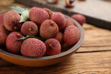 Photo of Fresh ripe lychee fruits in bowl on wooden table, closeup