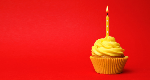 Photo of Delicious birthday cupcake with yellow cream and burning candle on red background. Space for text