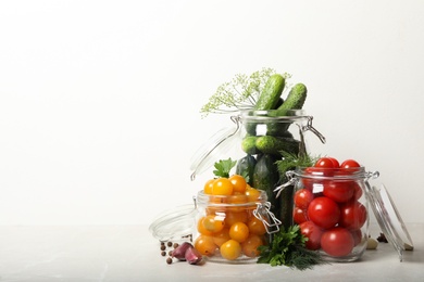Photo of Pickling jars with fresh vegetables on light table. Space for text