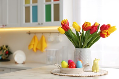 Photo of Easter decorations. Bouquet of tulips, painted eggs and bunny figure on table indoors. Space for text