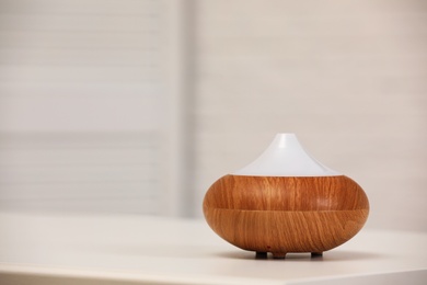 Photo of Modern essential oil diffuser on table indoors. Space for text