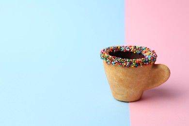 Photo of Delicious edible biscuit coffee cup decorated with sprinkles on color background, space for text