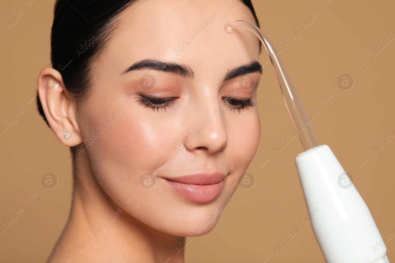 Photo of Woman using high frequency darsonval device on beige background, closeup