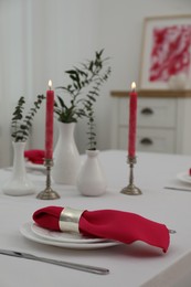 Photo of Table setting. Plates, pink napkin, cutlery, burning candles and vases with green branches in dining room