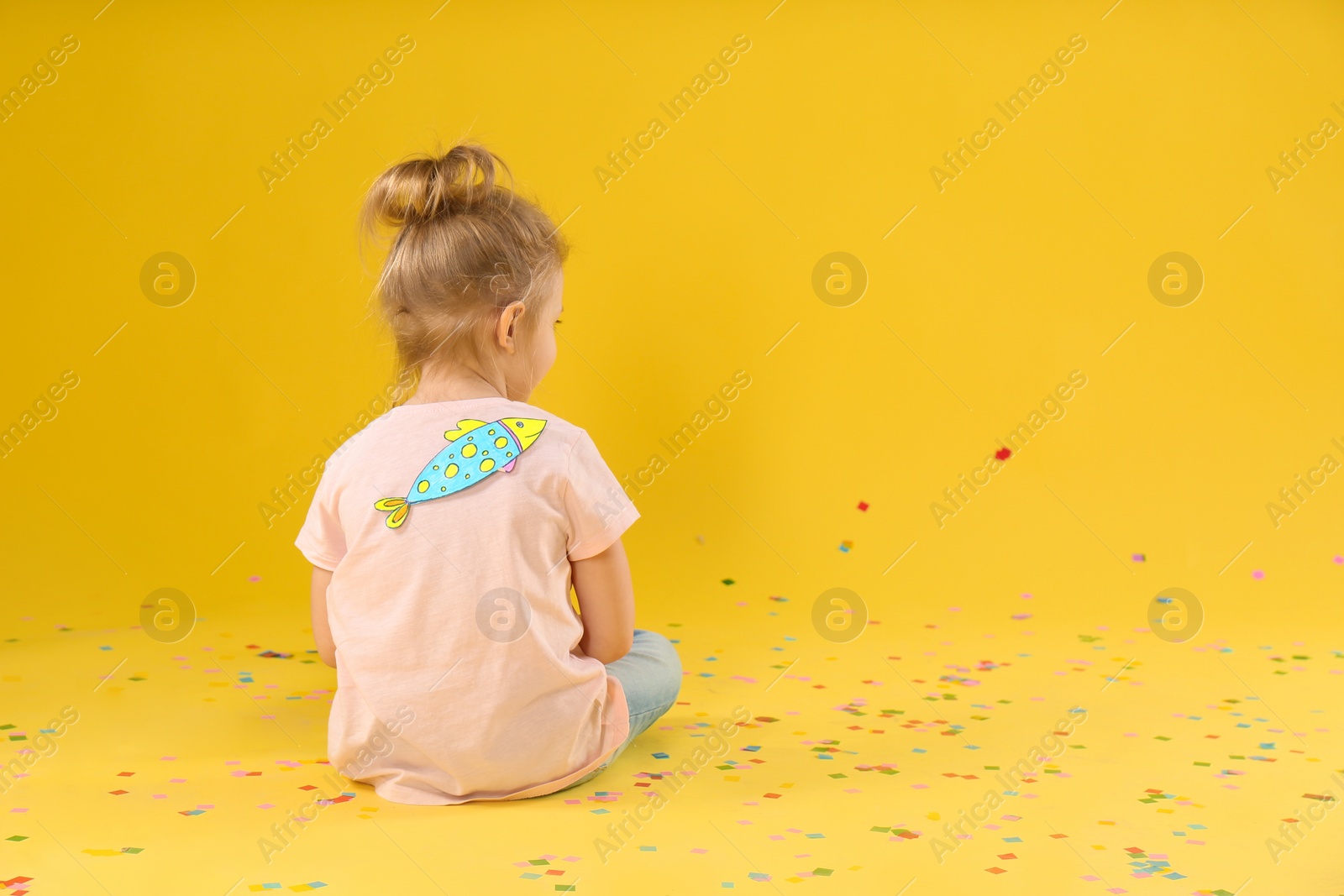 Photo of Little girl with paper fish on back against yellow background, space for text. April fool's day