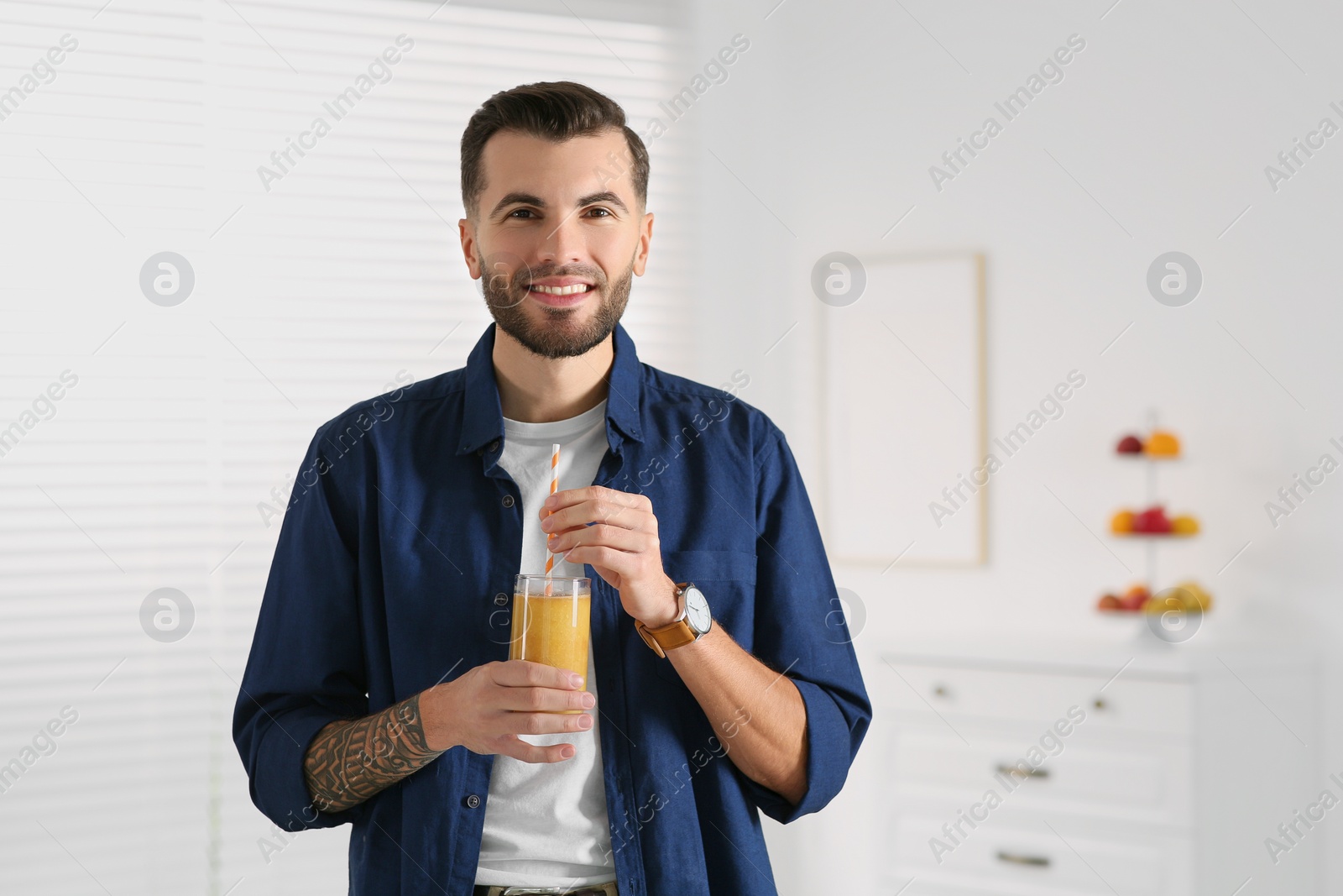 Photo of Handsome man with delicious smoothie at home. Space for text