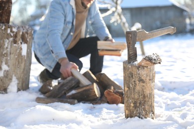 Man taking logs from pile outdoors on winter day. Metal axe in wooden log on snow, selective focus