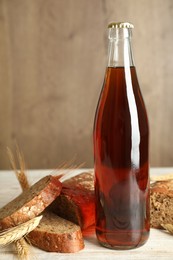 Bottle of delicious fresh kvass, spikelets and bread on white wooden table