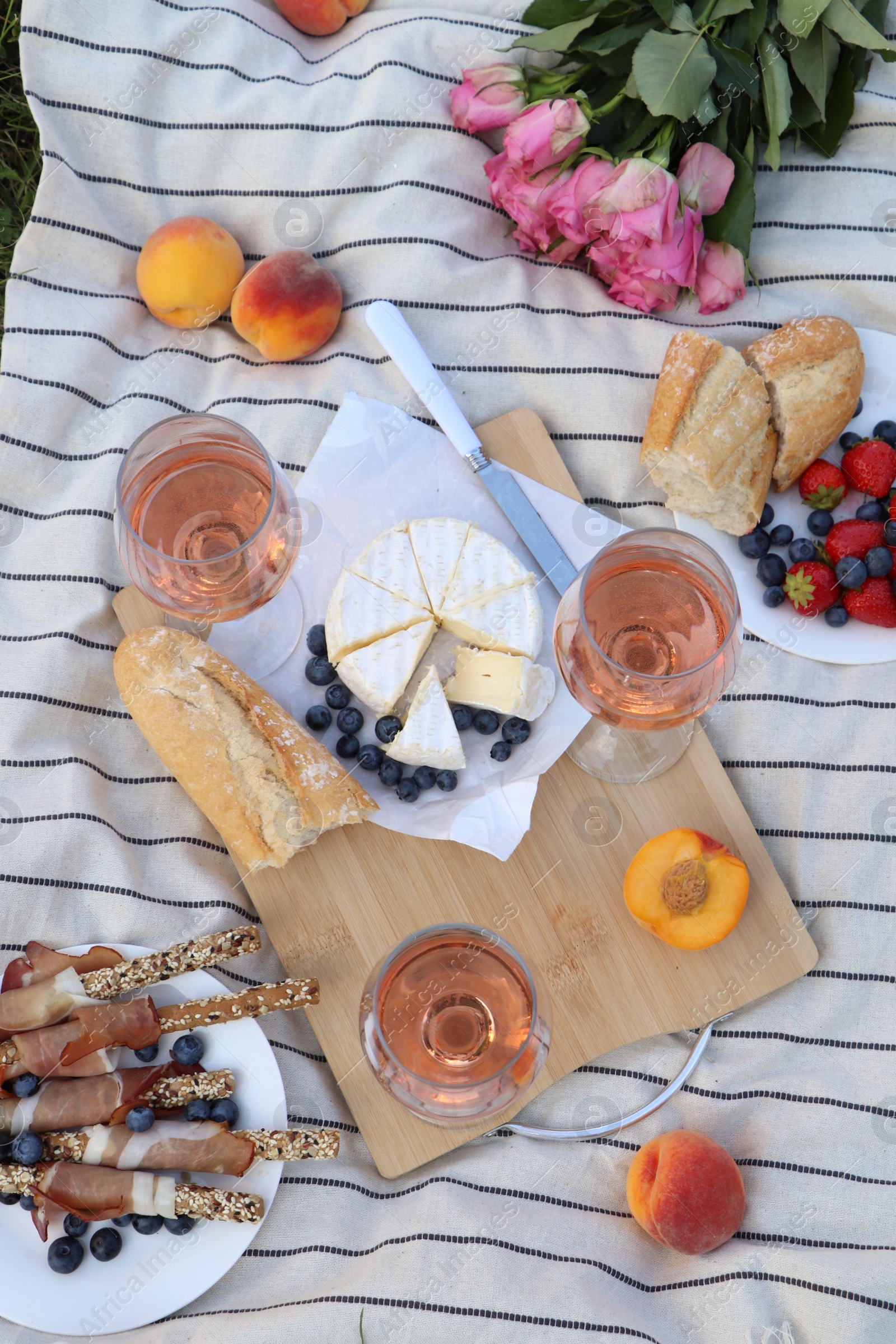 Photo of Glasses of delicious rose wine, flowers and food on white picnic blanket, flat lay