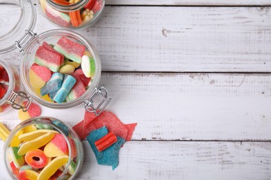 Photo of Tasty jelly candies in different jars on white wooden table, flat lay. Space for text