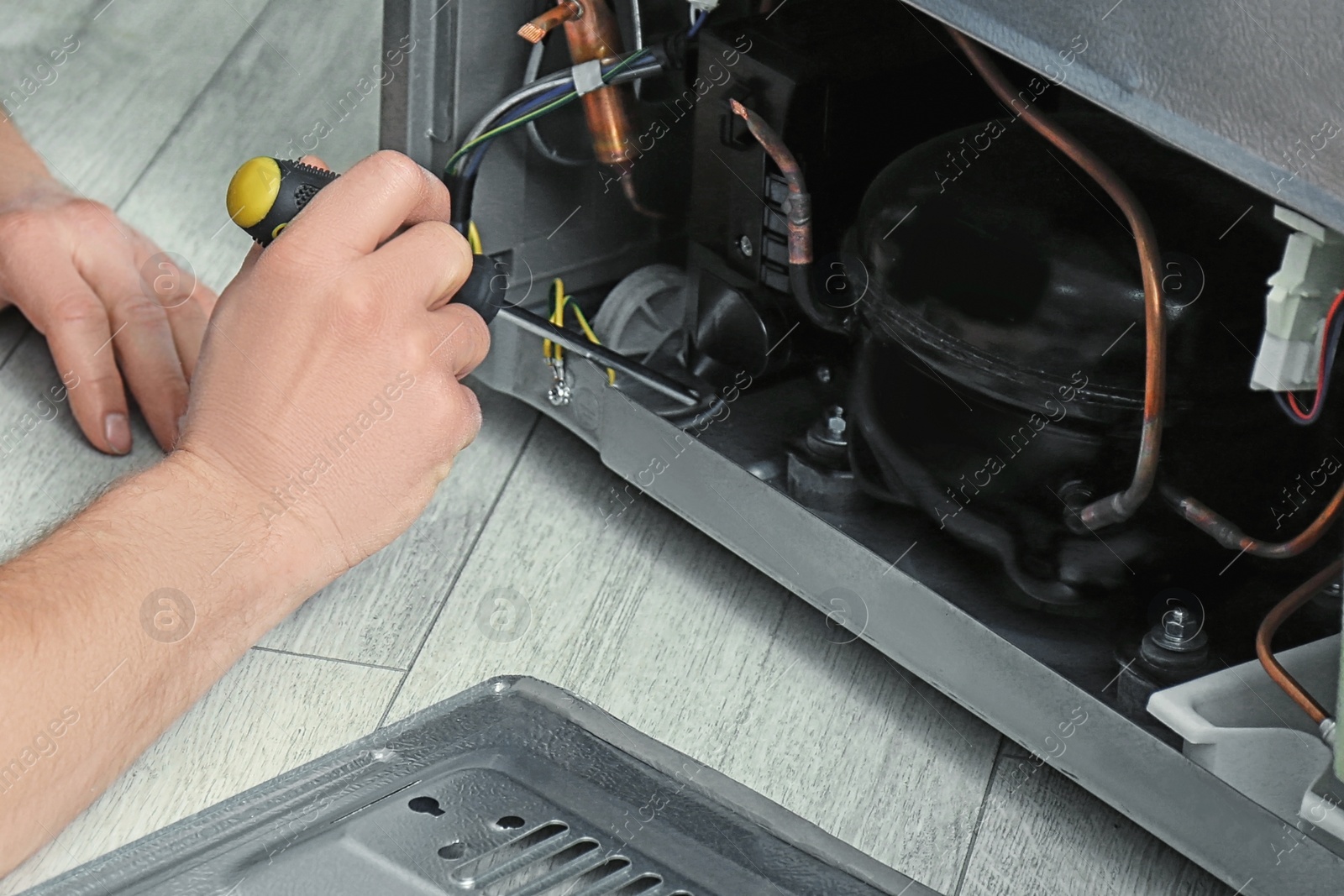 Image of Electrician with screwdriver fixing refrigerator indoors, closeup 