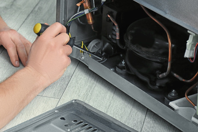 Electrician with screwdriver fixing refrigerator indoors, closeup 