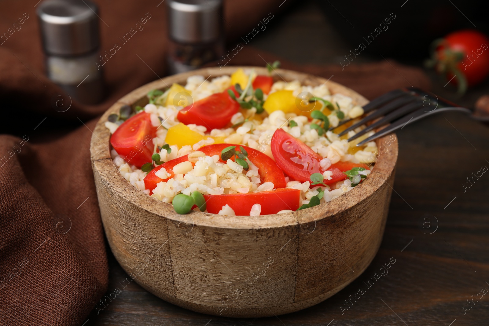 Photo of Cooked bulgur with vegetables in bowl on wooden table, closeup