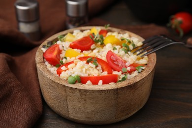 Cooked bulgur with vegetables in bowl on wooden table, closeup