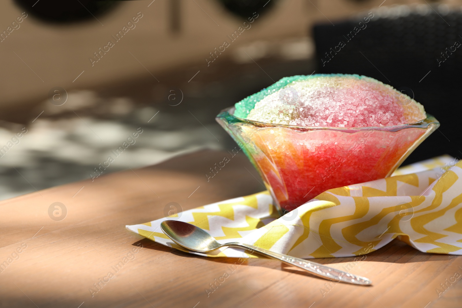 Photo of Rainbow shaving ice in glass dessert bowl and spoon on wooden table outdoors