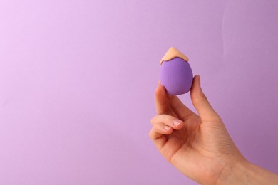 Photo of Woman holding makeup sponge with skin foundation on violet background, closeup. Space for text