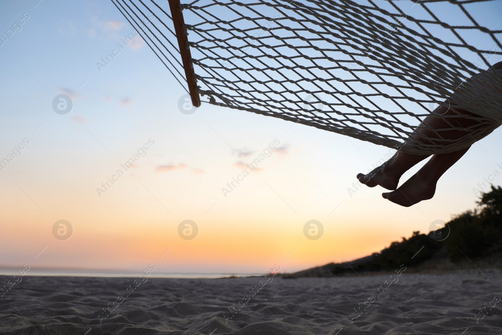 Photo of Young woman relaxing in hammock on beach at sunset, closeup