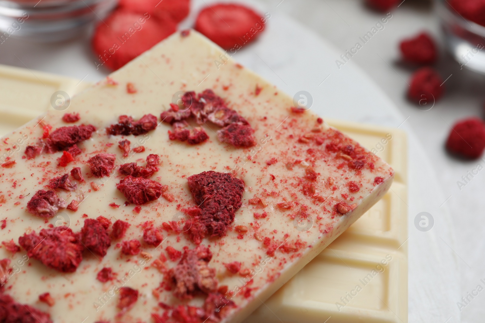 Photo of Chocolate bars with freeze dried raspberries on light marble board, closeup