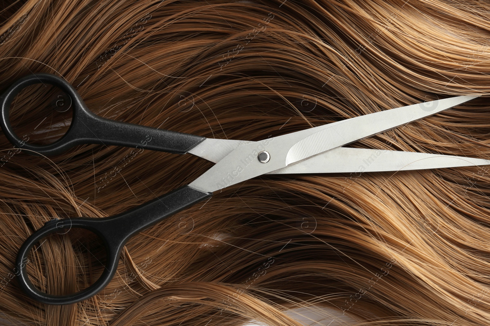 Photo of Scissors on brown wavy hair, top view. Hairdresser service
