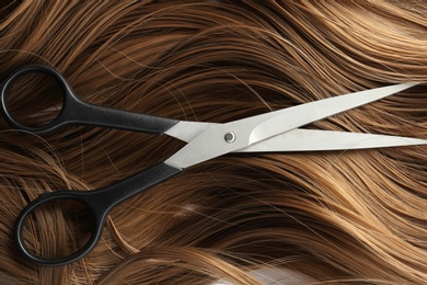 Photo of Scissors on brown wavy hair, top view. Hairdresser service