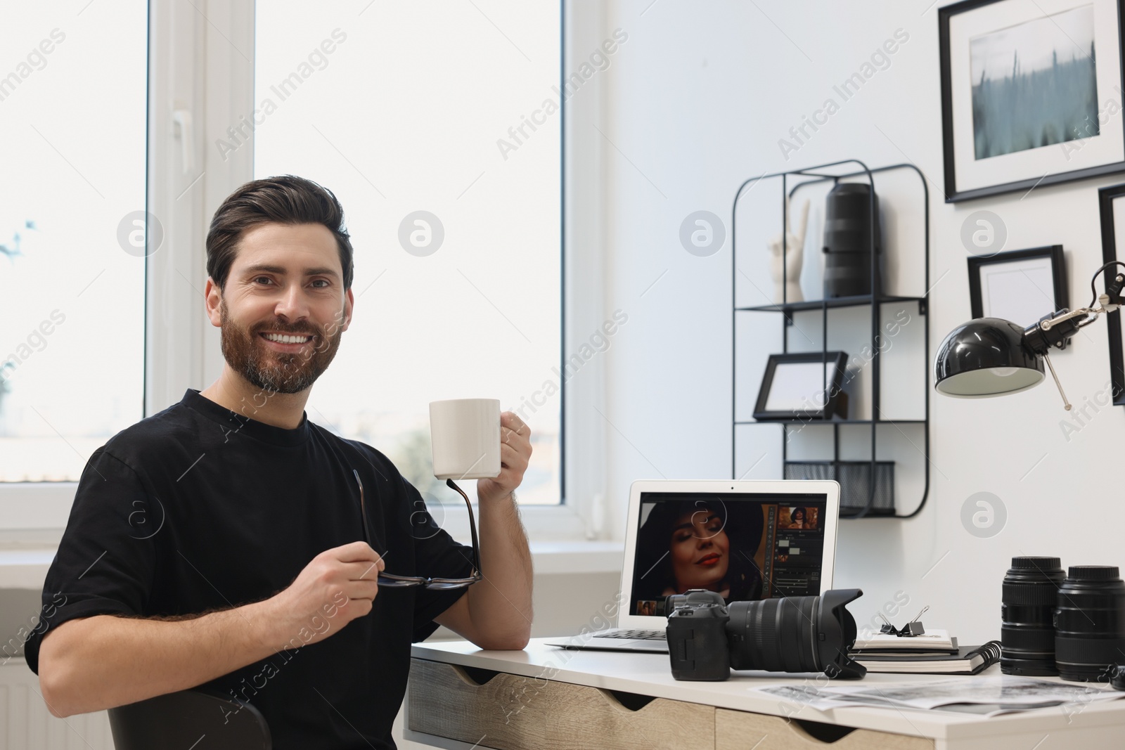 Photo of Professional photographer with cup of drink at table in office