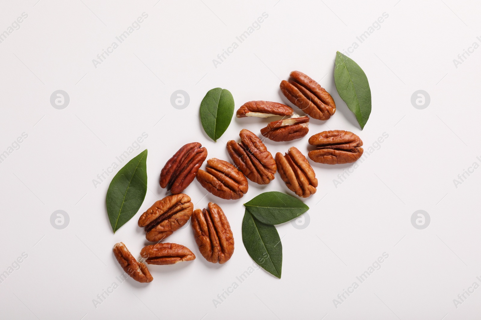 Photo of Delicious pecan nuts and green leaves on white background, flat lay