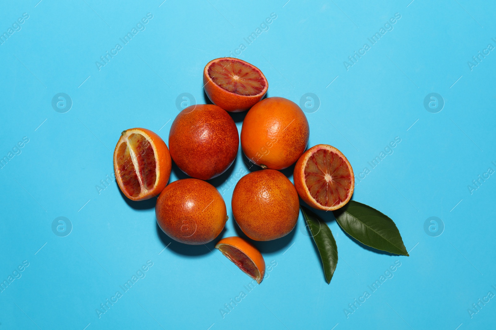 Photo of Many ripe sicilian oranges and leaves on light blue background, flat lay