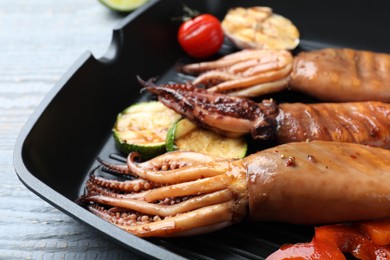 Photo of Tasty grilled squids with vegetables served on grey wooden table, closeup