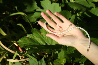 Photo of Woman holding elegant pearl necklace outdoors on sunny day, closeup. Space for text