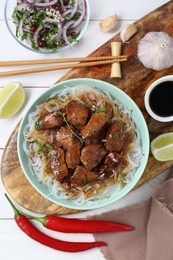 Bowl with pieces of soy sauce chicken and noodle on white wooden table, flat lay