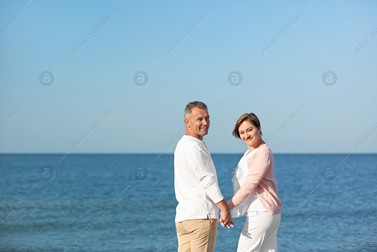 Photo of Happy mature couple holding hands at beach on sunny day