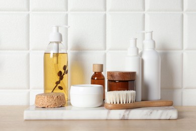 Different bath accessories and personal care products on wooden table near white tiled wall