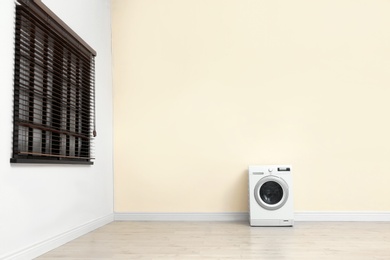 Photo of Washing machine near color wall in empty room, space for text. Laundry day