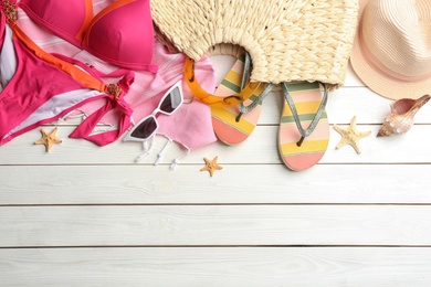 Photo of Bag with beach accessories and swimsuit on white wooden table, flat lay. Space for text