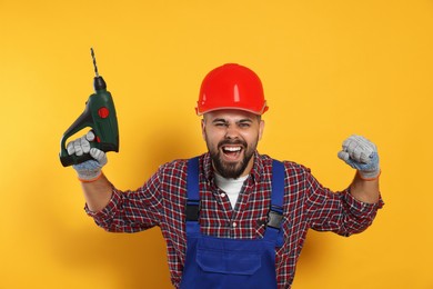 Photo of Emotional worker in uniform with power drill on yellow background