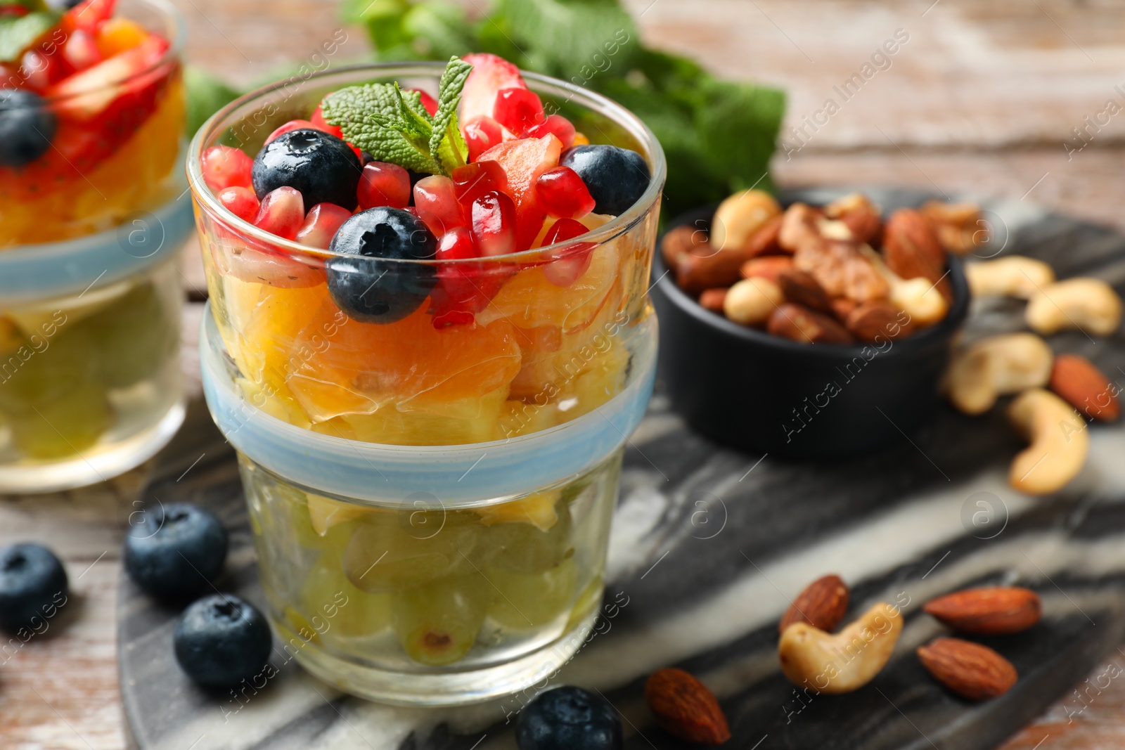 Photo of Delicious fruit salad, fresh berries, mint and nuts on wooden table