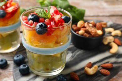 Photo of Delicious fruit salad, fresh berries, mint and nuts on wooden table