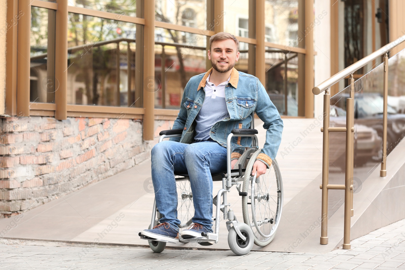 Photo of Young man in wheelchair using ramp at building outdoors