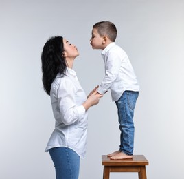 Beautiful mother kissing little son on white background
