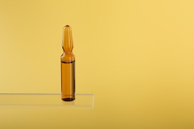 Photo of Glass ampoule with liquid on yellow background. Space for text