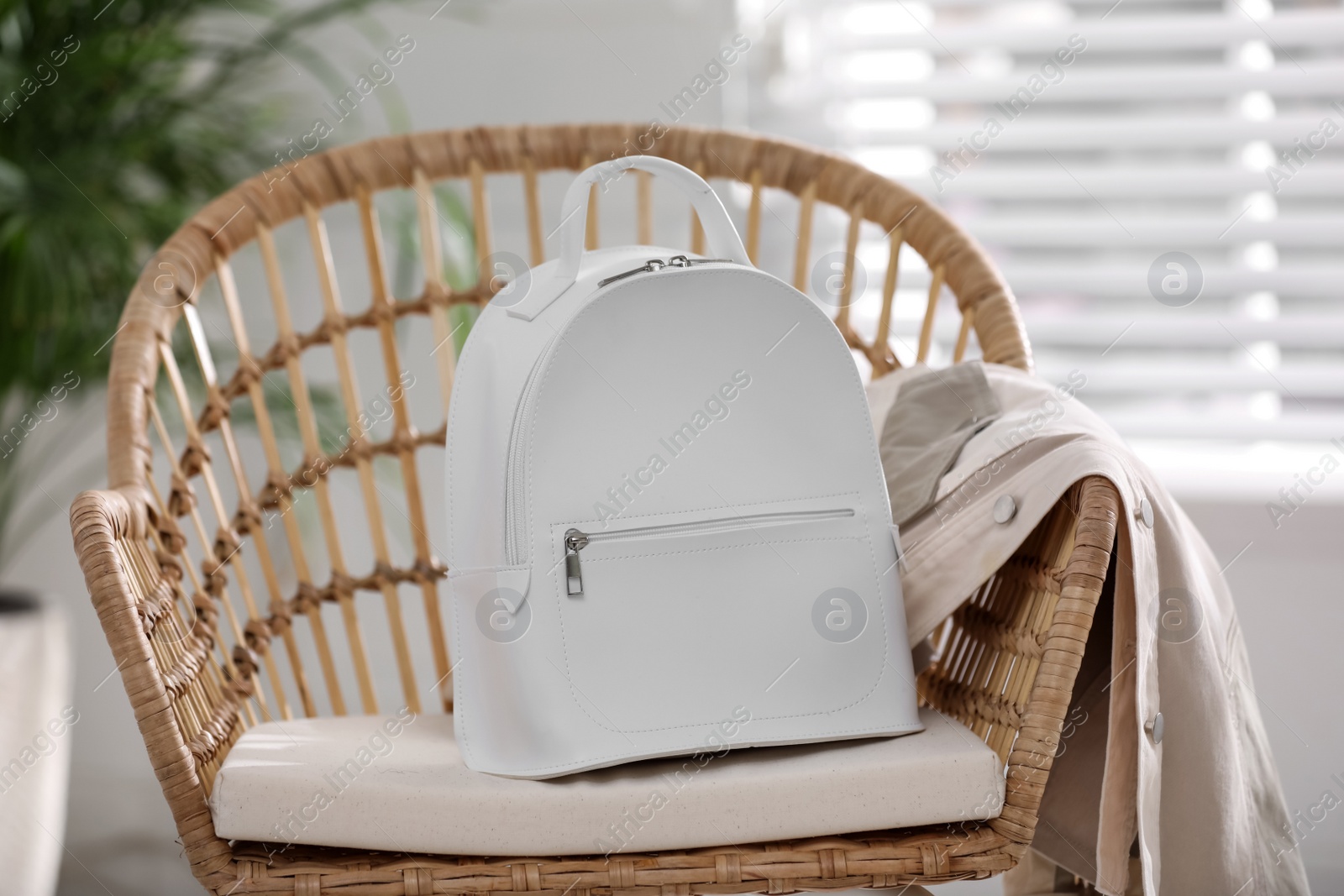 Photo of Stylish white backpack and jacket on wicker chair indoors