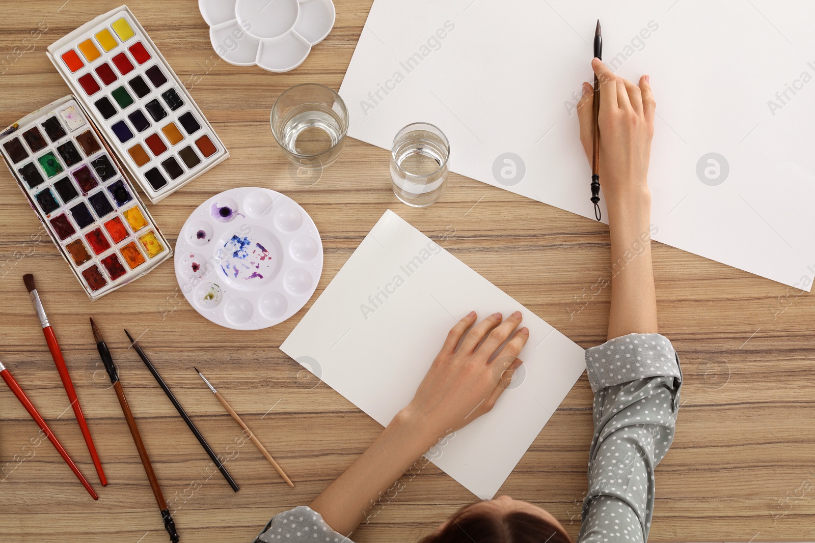 Photo of Woman painting with watercolor on blank paper at wooden table, top view