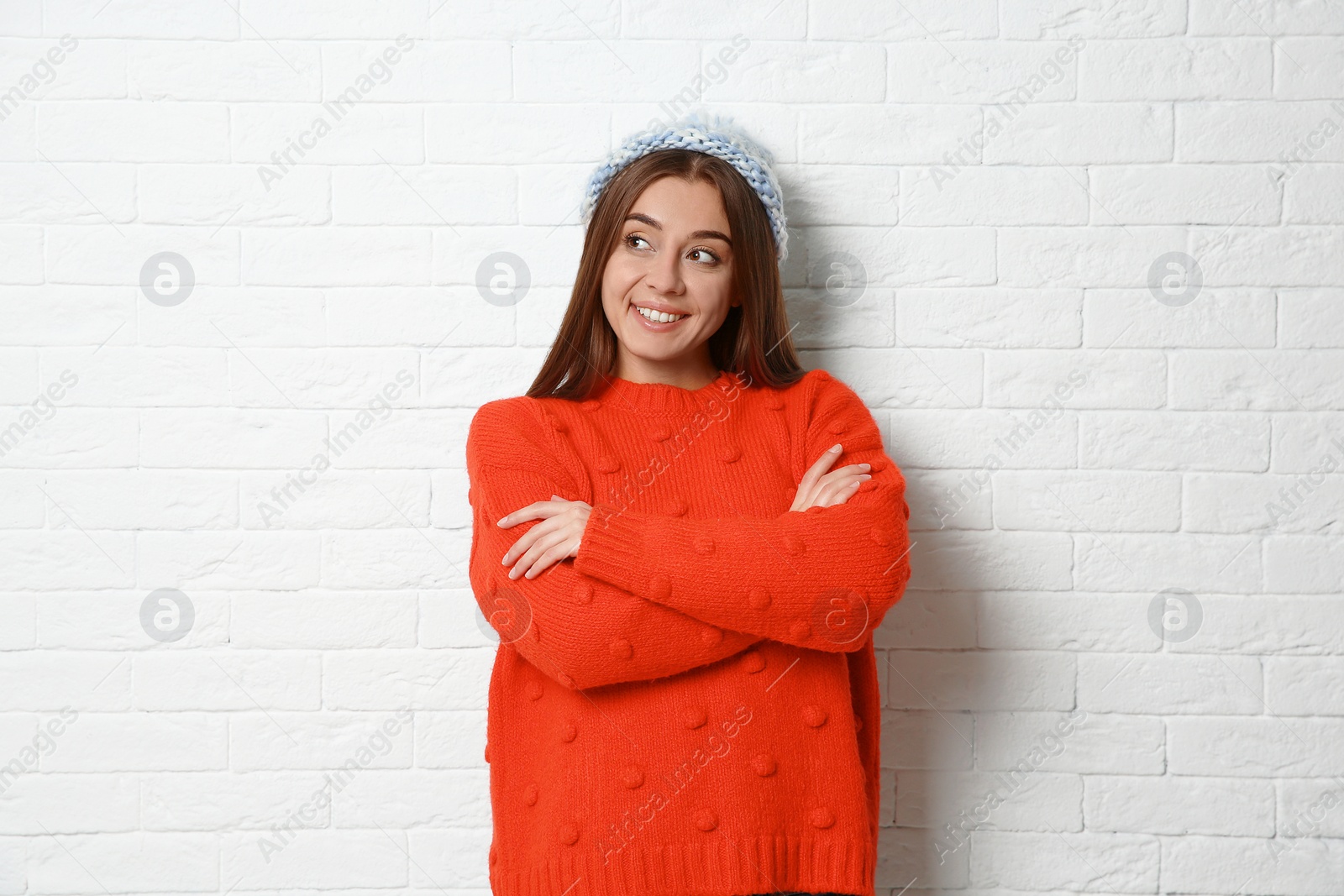 Photo of Beautiful young woman in warm sweater with hat near white brick wall