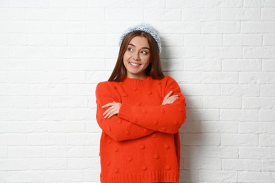 Beautiful young woman in warm sweater with hat near white brick wall