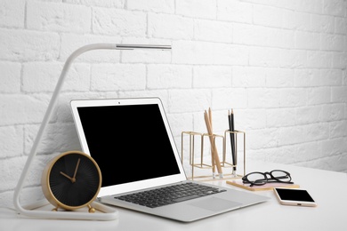 Photo of Modern workplace with laptop on table against brick wall. Mockup for design