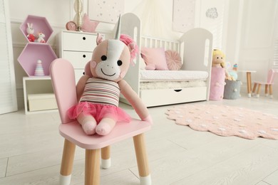 Photo of Cute unicorn toy on chair in baby room, space for text. Interior design