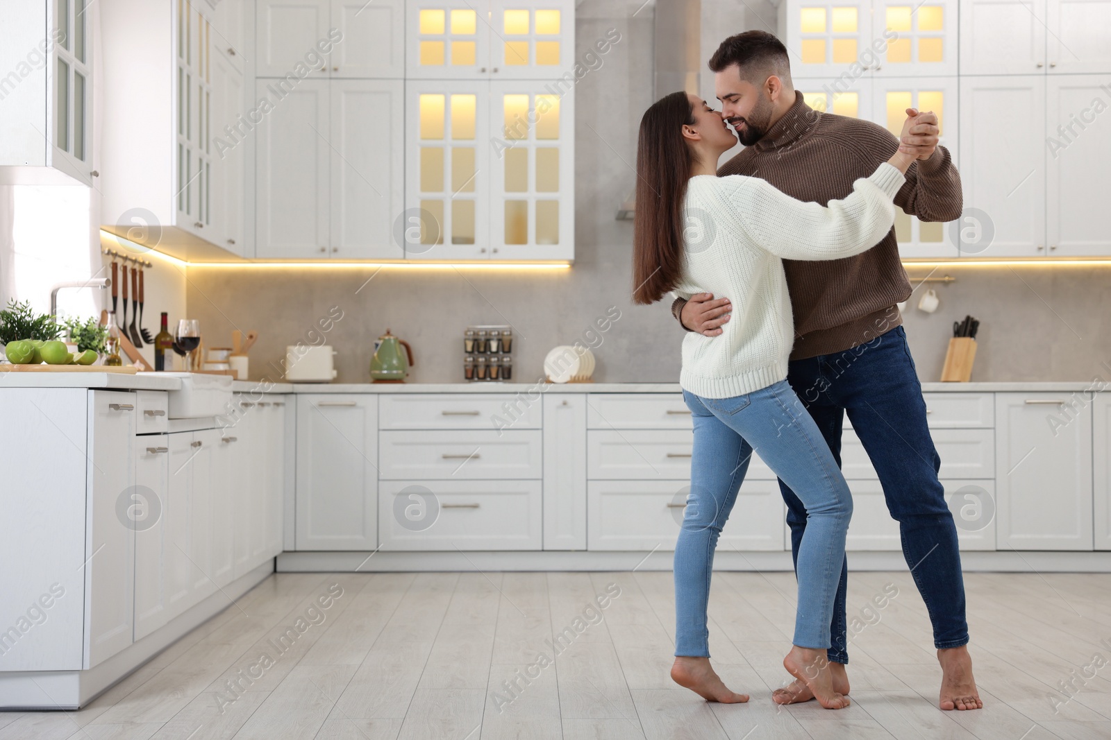 Photo of Affectionate young couple dancing and kissing in kitchen. Space for text
